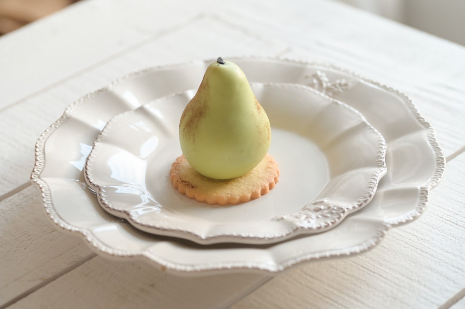 Poire en trompe-l’œil sur un sablé, dressée dans une assiette blanche